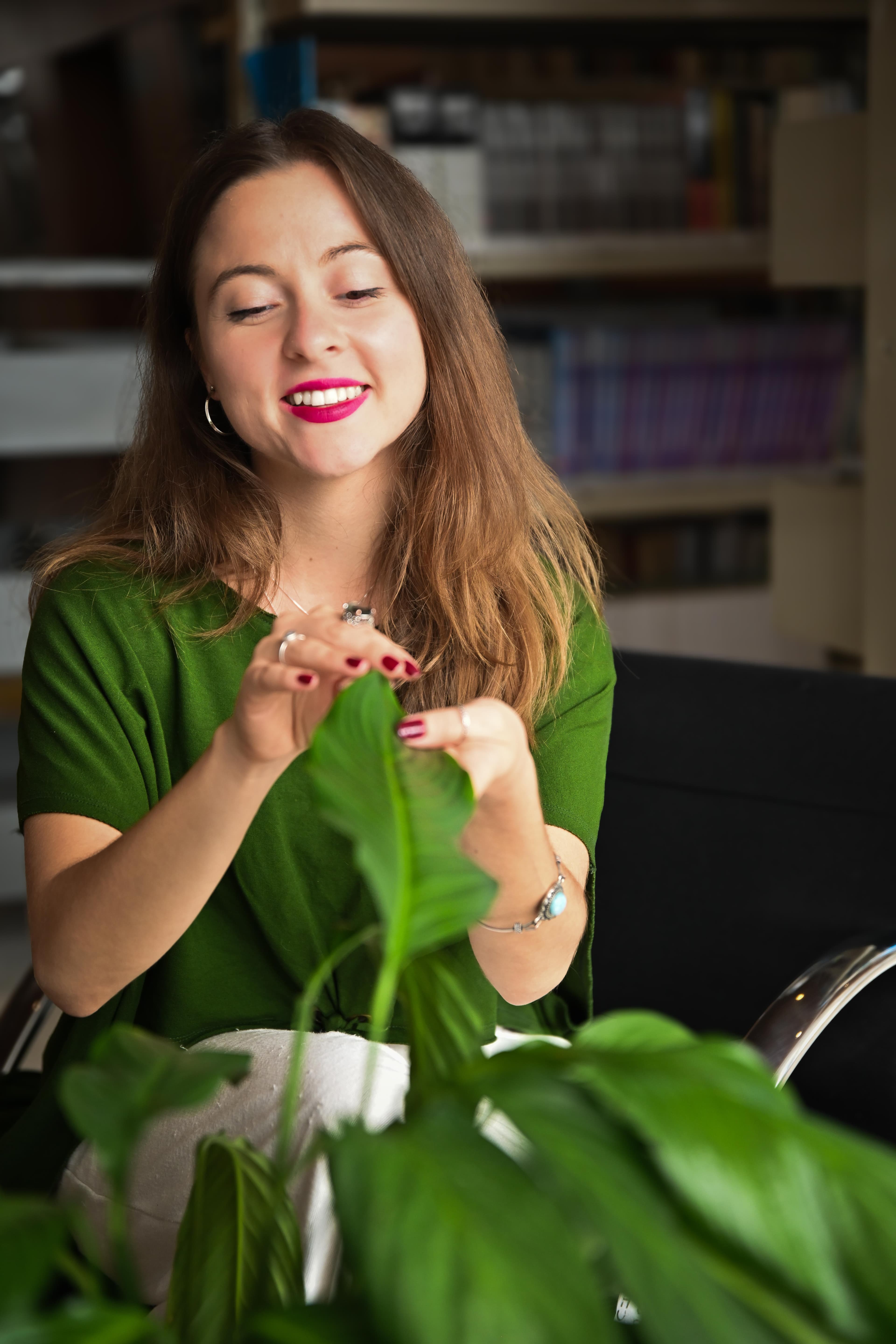 Geovana Grassmann, de blusa verde, sorrindo enquanto toca as folhas de uma planta